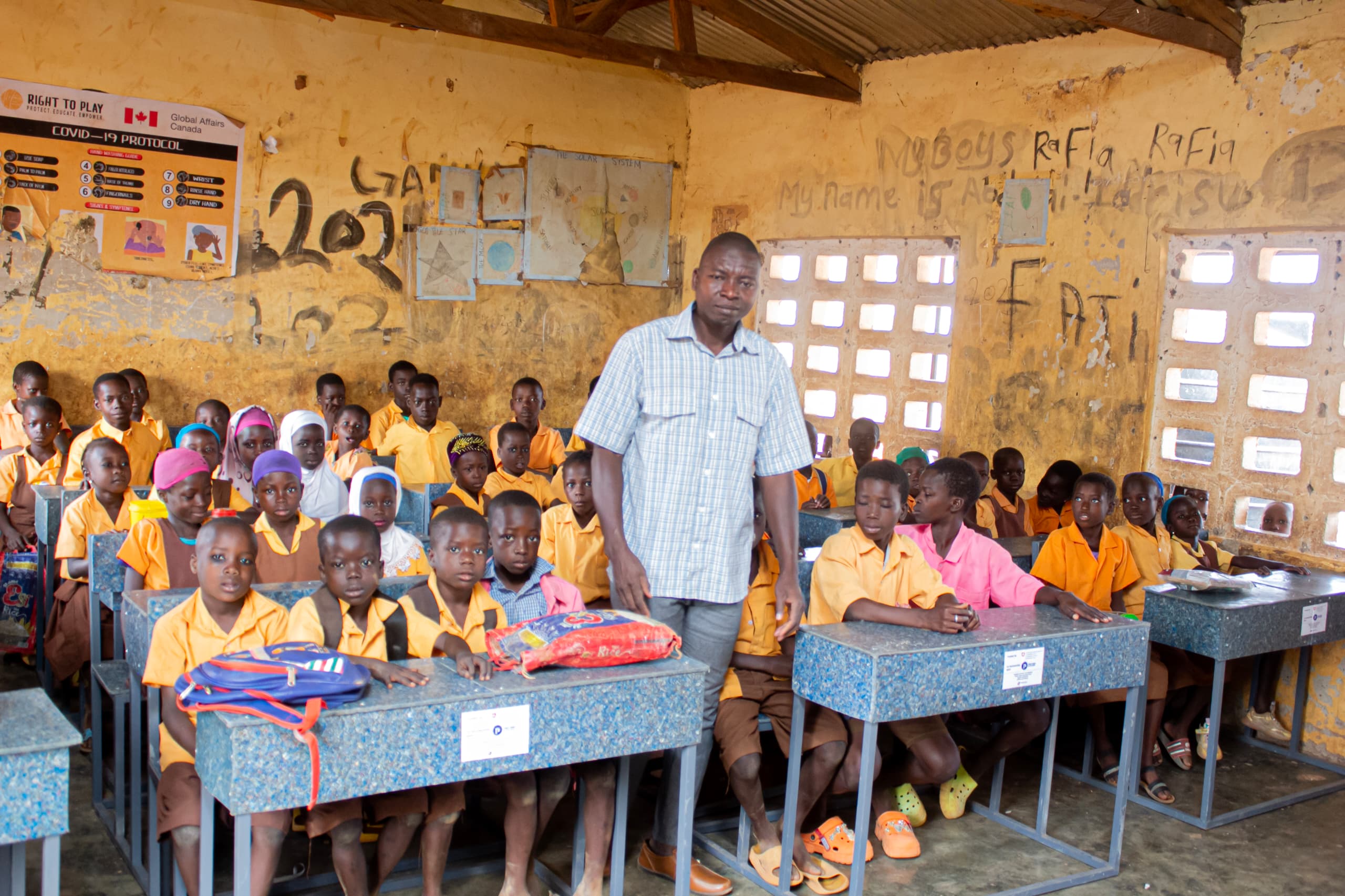 A teacher stands among students sitting at their new desks in a classroom in Northern Ghana