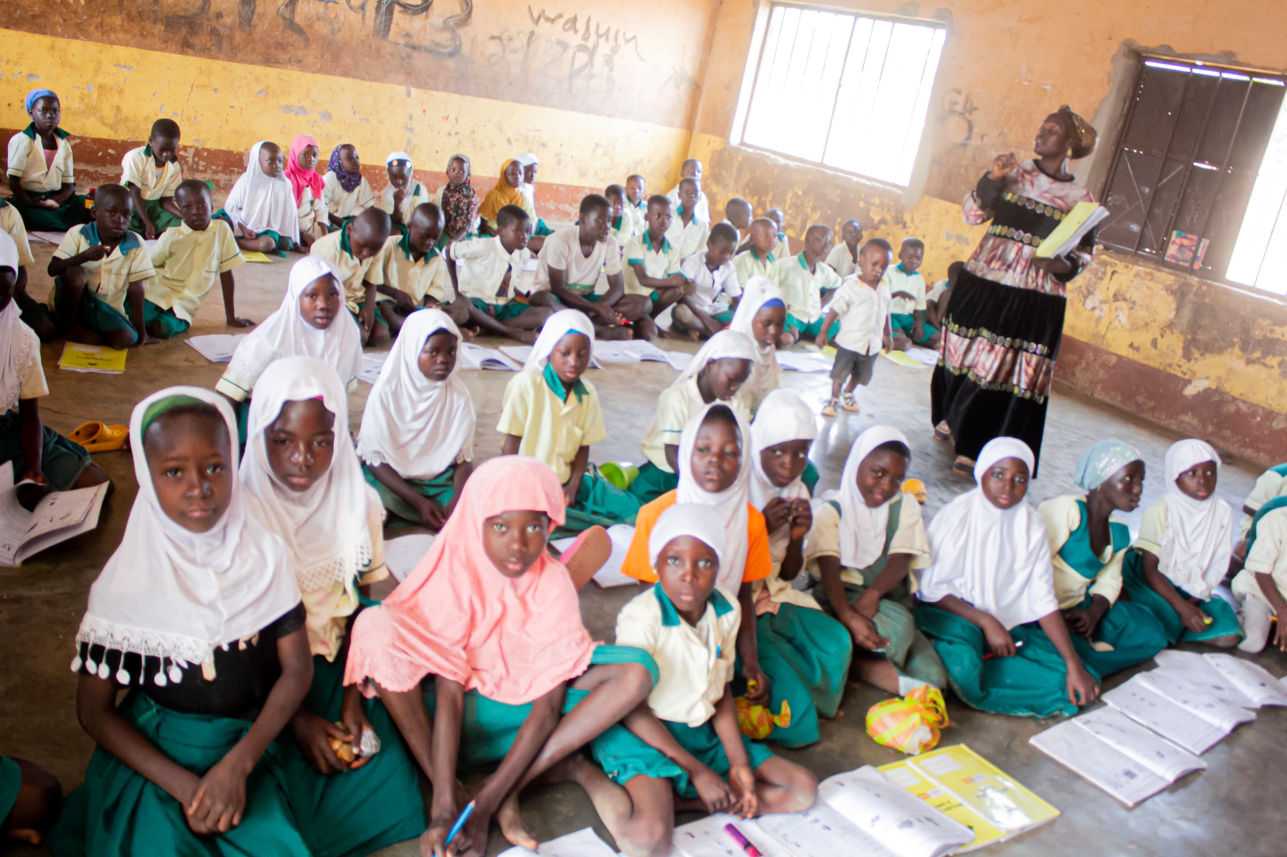 Girls with headscarves sitting on a bare classroom floor, learning without desks