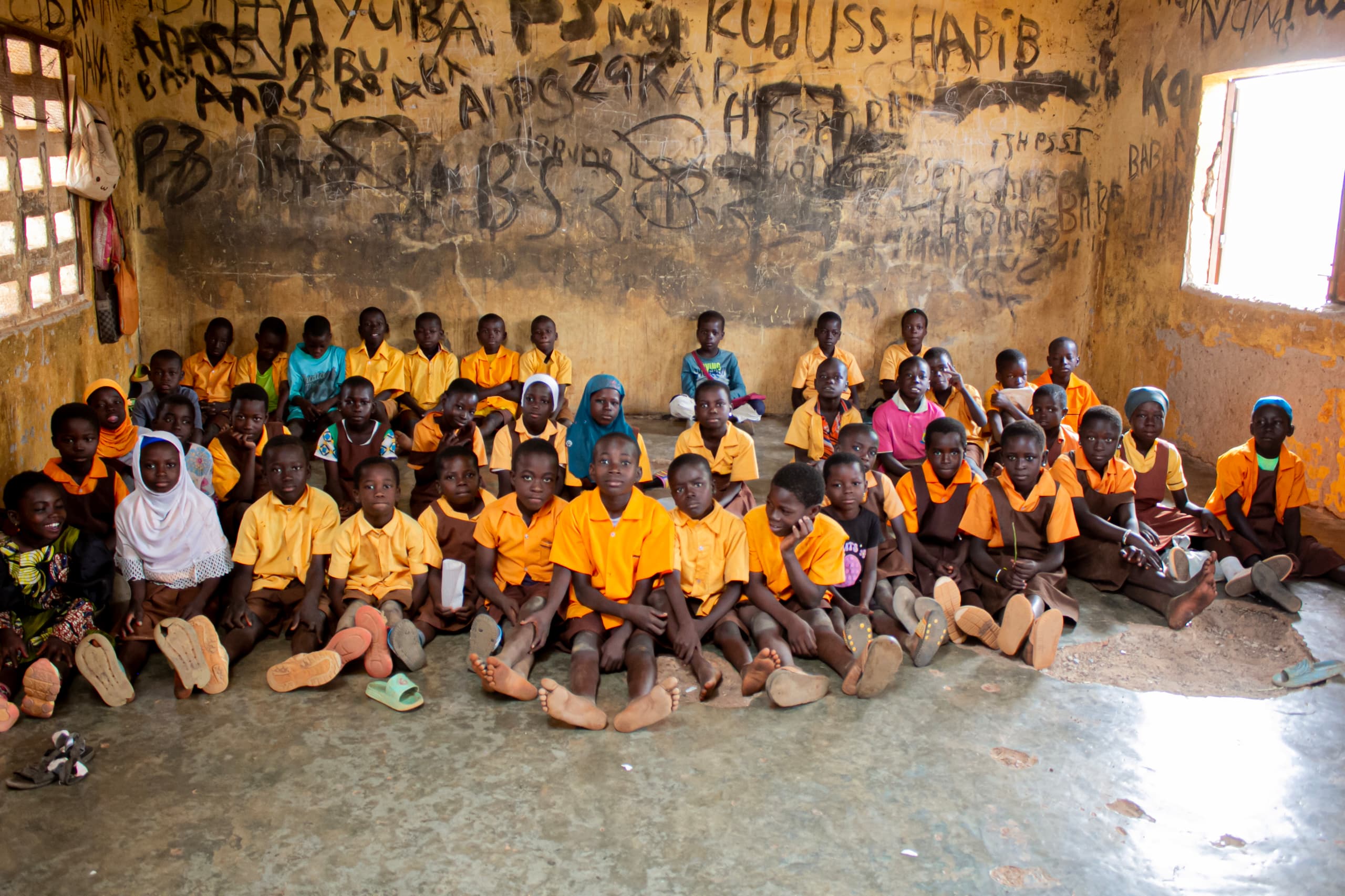 An entire classroom of children sitting on a bare floor with no desks in sight